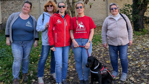 Rózsa Kata, Juhászné Mályi Edit, Végel Gabriella, Mali Andrea és Hajdu Mária, Frida, a frissen vizsgázott vakvezetőkutya, Andrea lába előtt ül.